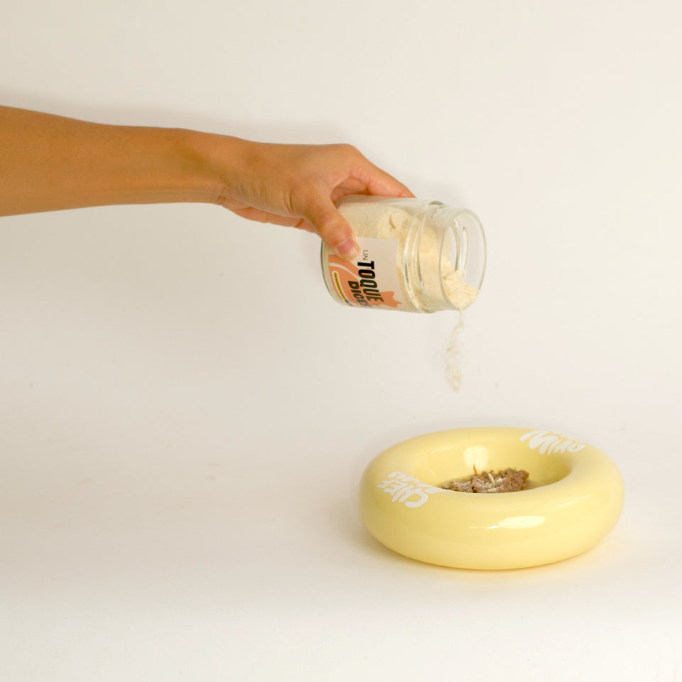 Una mano espolvorea Toque sobre la comida en un cuenco amarillo