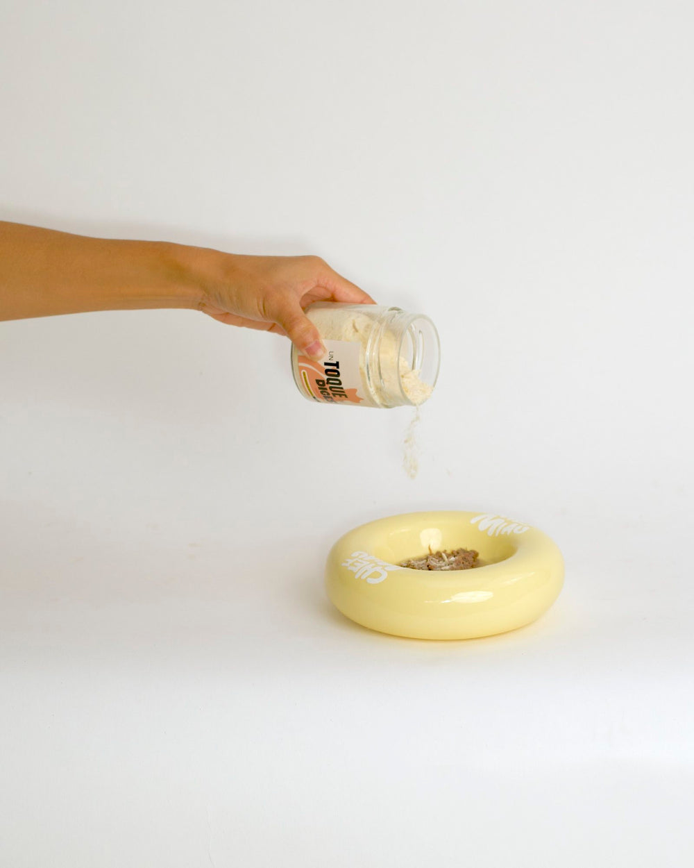 Una mano espolvorea Toque sobre la comida en un cuenco amarillo